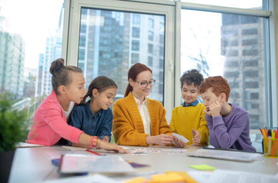 School,Games.,Group,Of,Schoolchildren,Sitting,Around,Their,Teacher,At